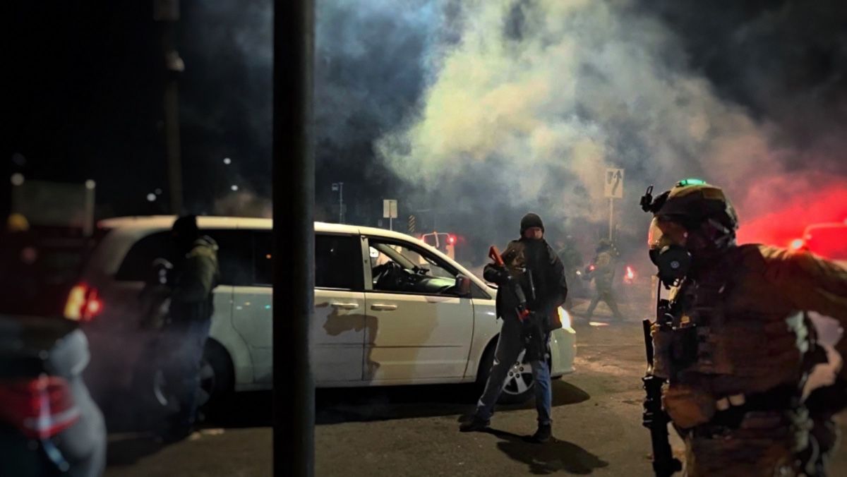 A police line in smoke at night, seen from behind the crowd